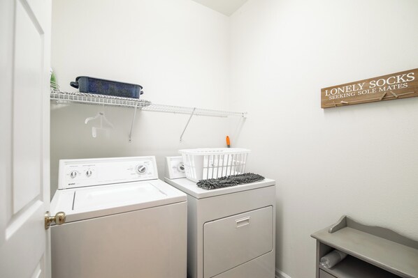 A laundry area with a washing machine, dryer, and a shelf with a basket and a mop.