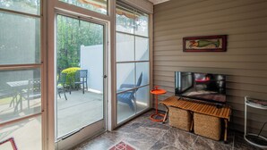A screened-in porch with a sliding glass door, a television, a small table, and outdoor furniture. - TB 94B Dog friendly Garden home in the peaceful True Blue community. (Pawleys island)