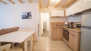 A modern kitchen with wooden cabinets, a built-in oven, and a refrigerator. There is a dining area with a table and chairs. - 🎖 Le Parmelan - apartment for 2 people in the heart of the old town (Annecy)