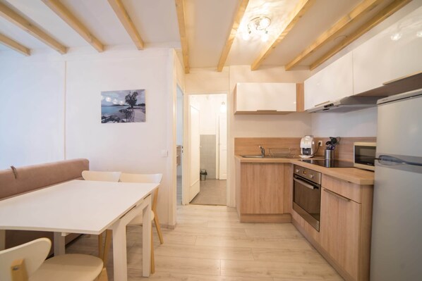 A modern kitchen with wooden cabinets, a built-in oven, and a refrigerator. There is a dining area with a table and chairs.