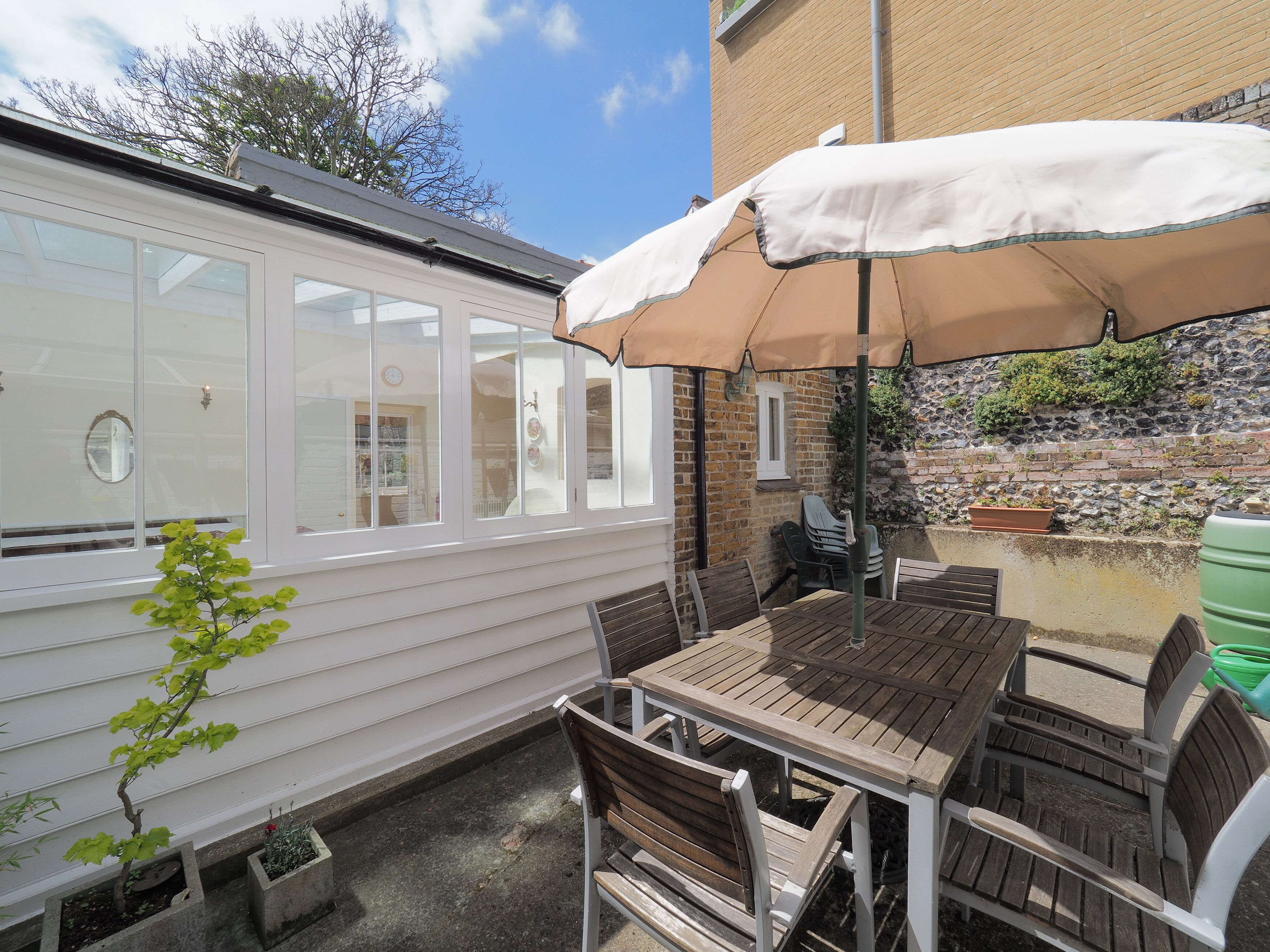A patio with a wooden table and chairs, an umbrella, and a white mobile home with large windows.