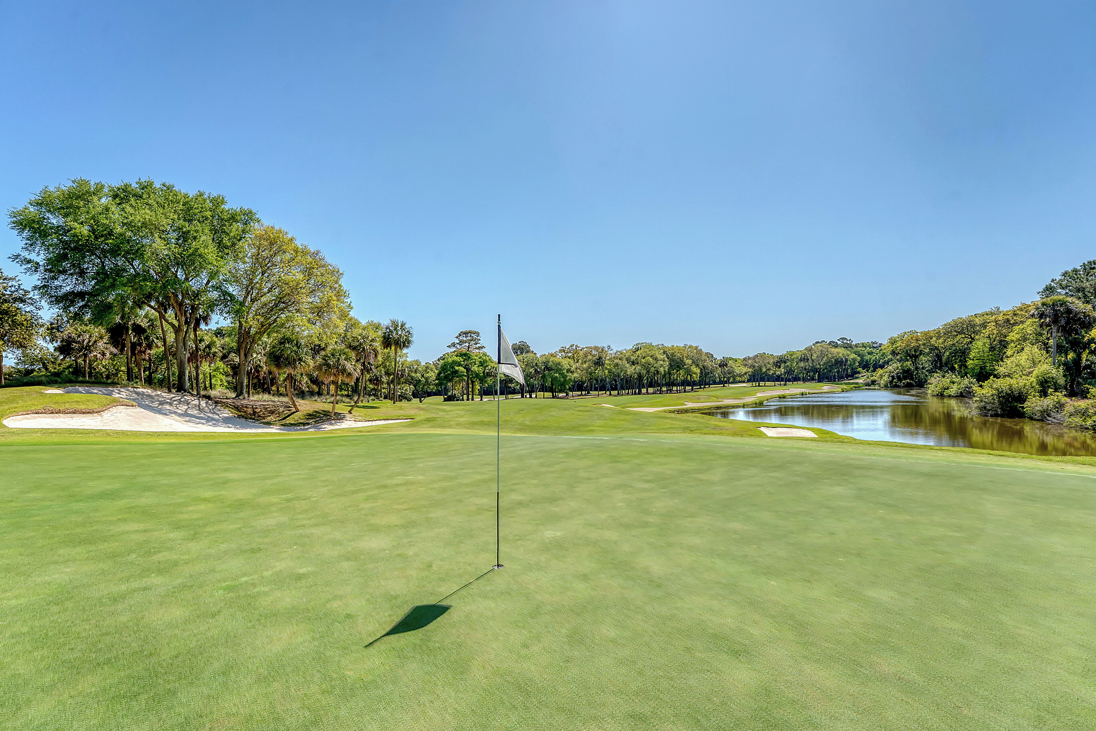 A golf course with a flagstick, sand bunkers, and a pond.