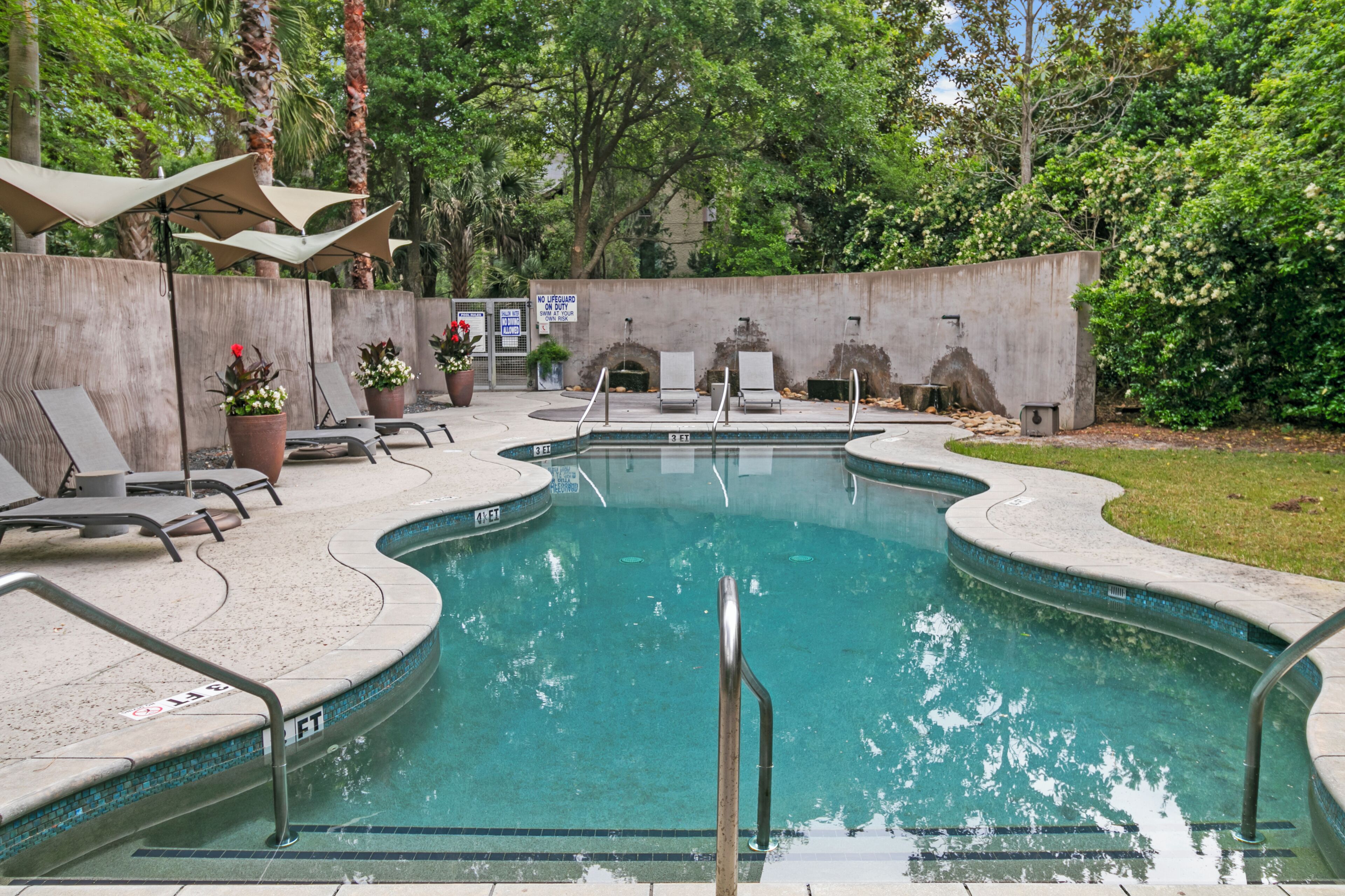 A pool area with lounge chairs, a concrete wall, and potted plants.