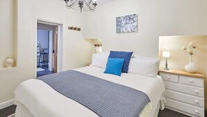 A hotel room with a large bed, a chandelier, a bedside table with a lamp, and a door leading to another room. - Host & Stay | Ocean Breeze (Scarborough)
