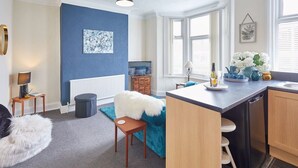 A modern kitchen with a central island, a dining area with a blue sofa, and a living space with a white fluffy chair. - Host & Stay | Rockpool (Scarborough)