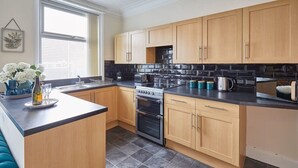 A modern kitchen with wooden cabinets, a black countertop, and a tiled floor. - Host & Stay | Rockpool (Scarborough)