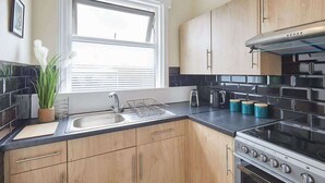 A modern kitchen with wooden cabinets, a stainless steel stove, and a window with blinds.