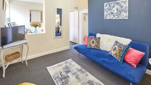 A living room with a blue sofa, a flat-screen TV, a small table, and a patterned rug.