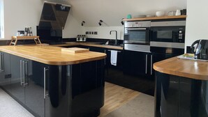 A modern kitchen with black cabinets, a wooden countertop, and stainless steel appliances including a Bosch oven and microwave. - Spacious One Bed Deluxe Apartment in Daventry (Daventry)