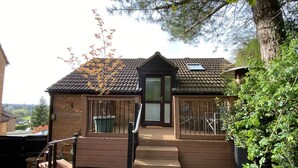 A house with a wooden deck, a glass door entrance, and a small garden area with potted plants. - Spacious One Bed Deluxe Apartment in Daventry (Daventry)