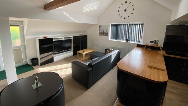 A modern living room with a TV, black sofa, wooden coffee table, and a kitchen area with a stove. - Spacious One Bed Deluxe Apartment in Daventry (Daventry)