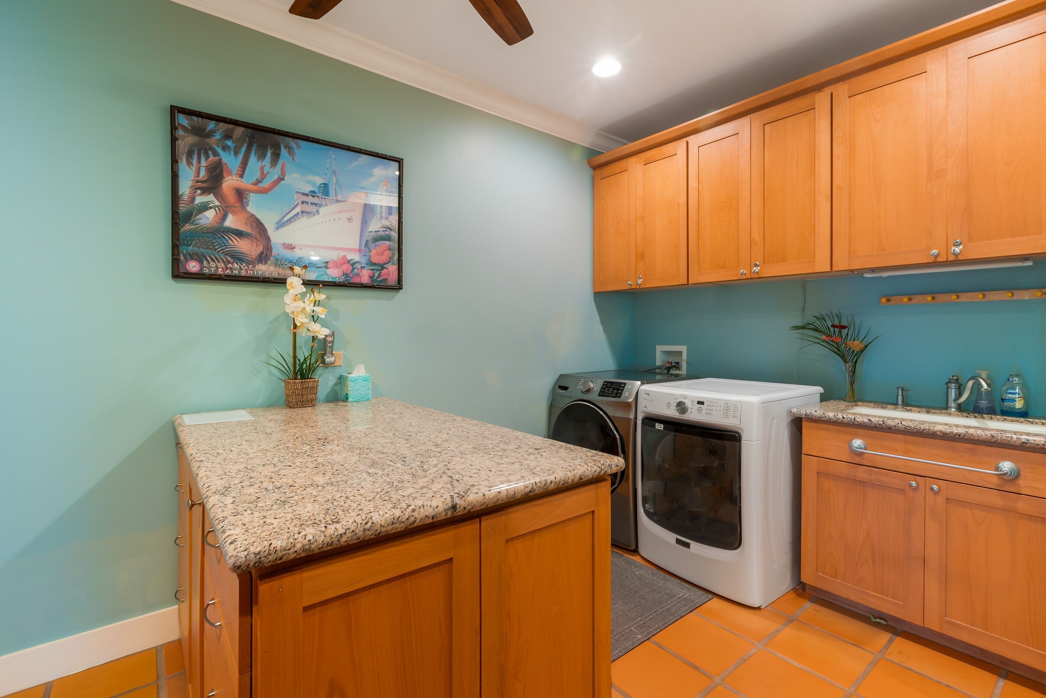 A kitchen with wooden cabinets, a granite countertop, a washing machine, and a painting on the wall.