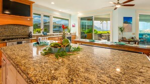 A spacious kitchen with granite countertops, a large island, and a dining area with a view. - Hawaii Life Rentals Presents Hale Ohana Nui (Princeville)