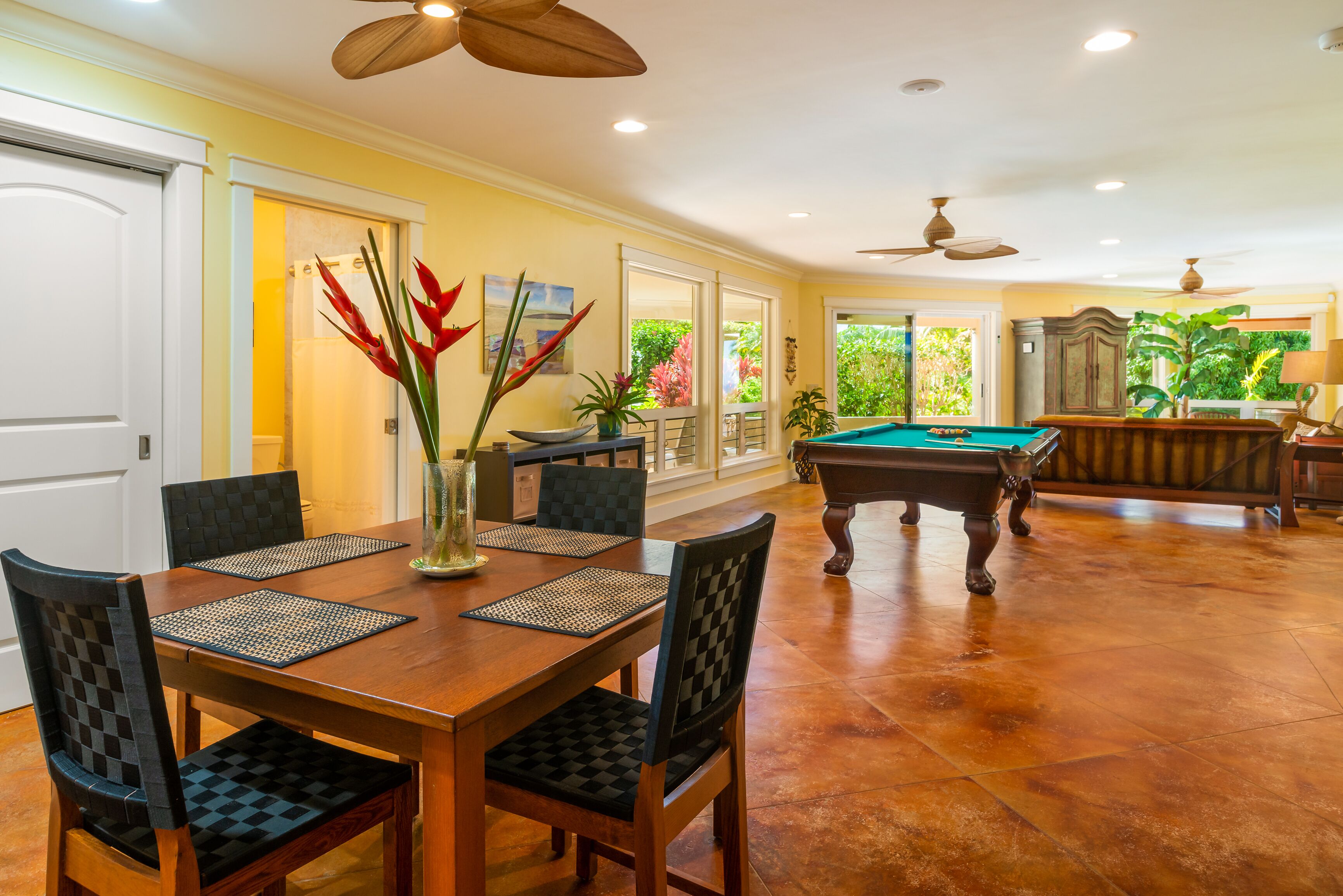 A dining area with a pool table, chairs, and a vase with flowers.