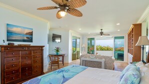 A bedroom with a bed, a dresser, a desk, and a view of the outdoors. - Hawaii Life Rentals Presents Hale Ohana Nui (Princeville)