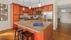 Una cocina moderna con armarios de madera, encimeras de granito, electrodomésticos de acero inoxidable e iluminación colgante.