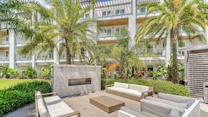 Un espace extérieur aménagé en terrasse, doté de mobilier contemporain, d’une cheminée en pierre et d’une végétation luxuriante.