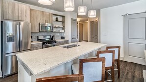 Une cuisine moderne dotée d’appareils électroménagers en acier inoxydable, d’un plan de travail en granit et de chaises en bois.