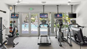 Une salle de sport équipée de tapis de course, de ballons d’exercice et offrant une vue sur la piscine.