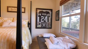 Et soveværelse med en seng, en bænk med håndklæder, en indrammet sportsjersey og et vindue med udsigt.