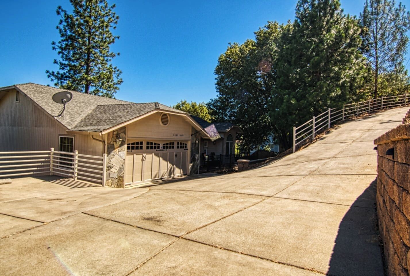 A ranch-style building with a garage, a satellite dish, and a fenced driveway.
