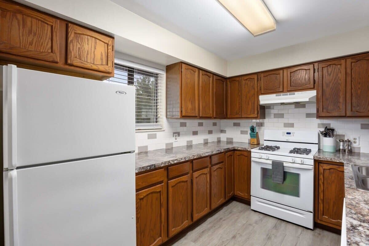 Una cocina con armarios de madera, un refrigerador blanco, una estufa y un salpicadero de azulejos.