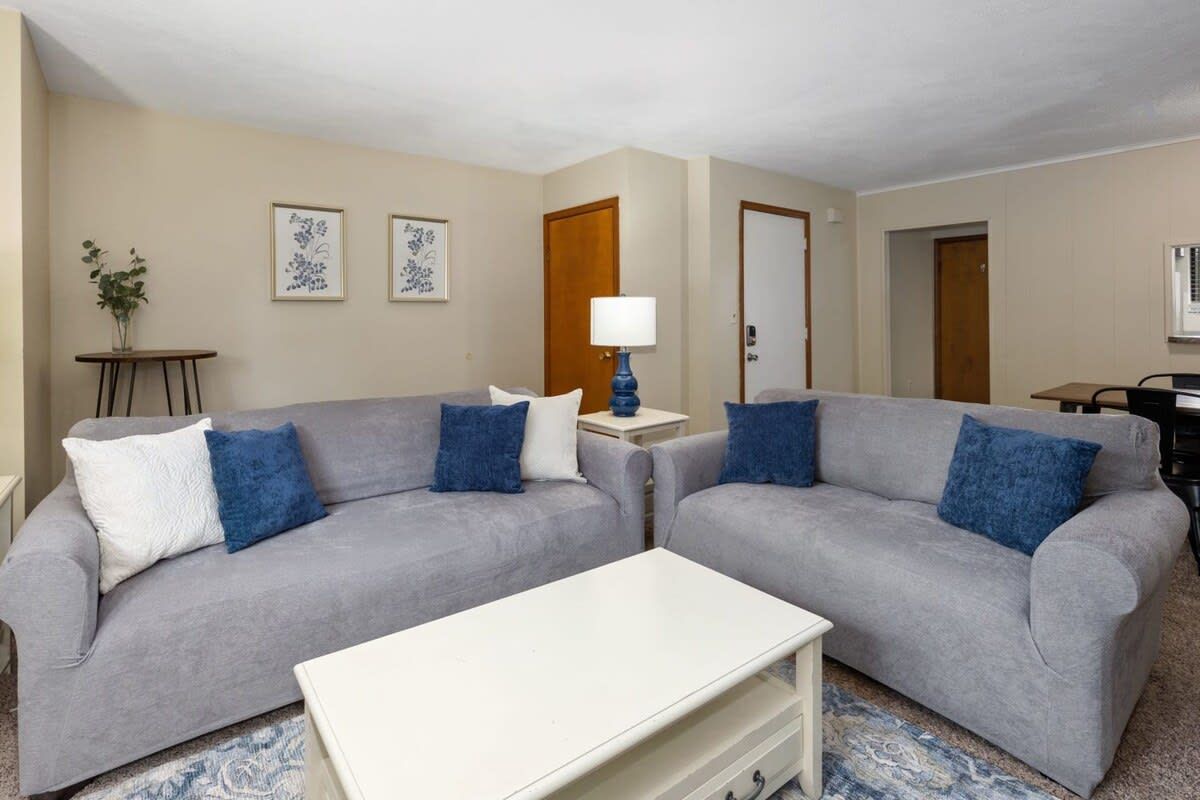 Una sala de estar con dos sofás grises, una mesa de centro blanca y una lámpara azul.