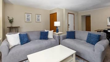Una sala de estar con dos sofás grises, una mesa de centro blanca y una lámpara azul.