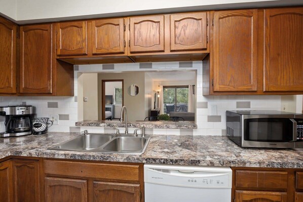 Una cocina con armarios de madera, encimera de granito, pileta de acero inoxidable y microondas integrado.