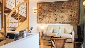 Ein Wohnzimmer mit einer Couch, einem Couchtisch, einem Korbstuhl, einer Wandteppich und einer Holztreppe.