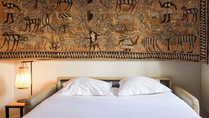 Ein Bett mit weißer Bettwäsche, ein Kopfteil mit einem gemusterten Wandteppich und eine Nachttischlampe.