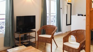 Ein Wohnzimmer mit Fernseher, Korbstühlen, einem Holztisch und einem Balkon mit Aussicht.