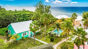 A turquoise house with a pool, surrounded by palm trees and a view of the ocean. - 20 Steps to the Beach  -SUMMER DISCOUNT- (Grand Cayman)
