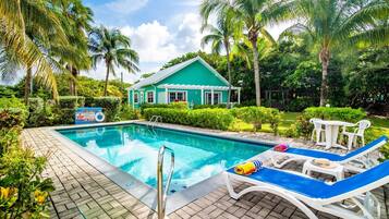 A swimming pool with lounge chairs, a lifeguard sign, and a house in the background.