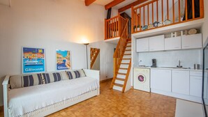 Une pièce confortable avec un canapé, un lave-linge et un escalier menant à une mezzanine.