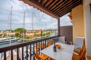 A balcony with a table and chairs overlooking a marina with boats and buildings. - Nice Apt In Front Of The Marina In Grimaud (Grimaud)