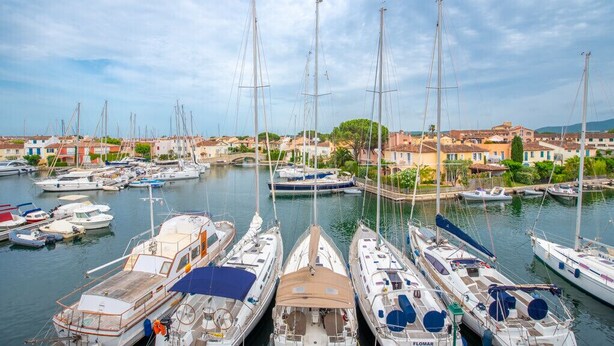 Un port de plaisance où sont amarrés de nombreux voiliers, entouré de bâtiments et de verdure.