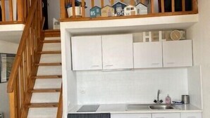 Une cuisine de taille réduite avec des meubles blancs, un escalier en bois et une petite fenêtre.