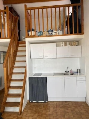 A compact kitchen with white cabinets, a wooden staircase, and a small window.