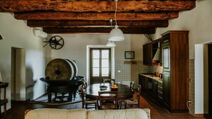 A rustic kitchen with a large stove, wooden cabinets, and a dining area with a round table and chairs. - The olive house is located in the grounds of the historic Villa Meleto estate (Toscana)