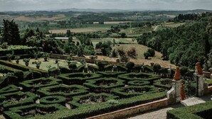 A landscaped garden with geometric hedges and statues, overlooking a rural landscape with fields and trees. - The olive house is located in the grounds of the historic Villa Meleto estate (Toscana)
