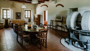 A rustic dining area with a wooden table and chairs, a fireplace, and a cozy seating area with a sofa and chairs. - The olive house is located in the grounds of the historic Villa Meleto estate (Toscana)