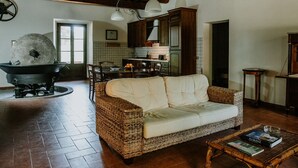 A cozy living room with a wicker sofa, a coffee table with books, a stone stove, and wooden cabinets. - The olive house is located in the grounds of the historic Villa Meleto estate (Toscana)