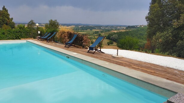 A swimming pool with lounge chairs and a view of a countryside landscape. - The olive house is located in the grounds of the historic Villa Meleto estate (Toscana)