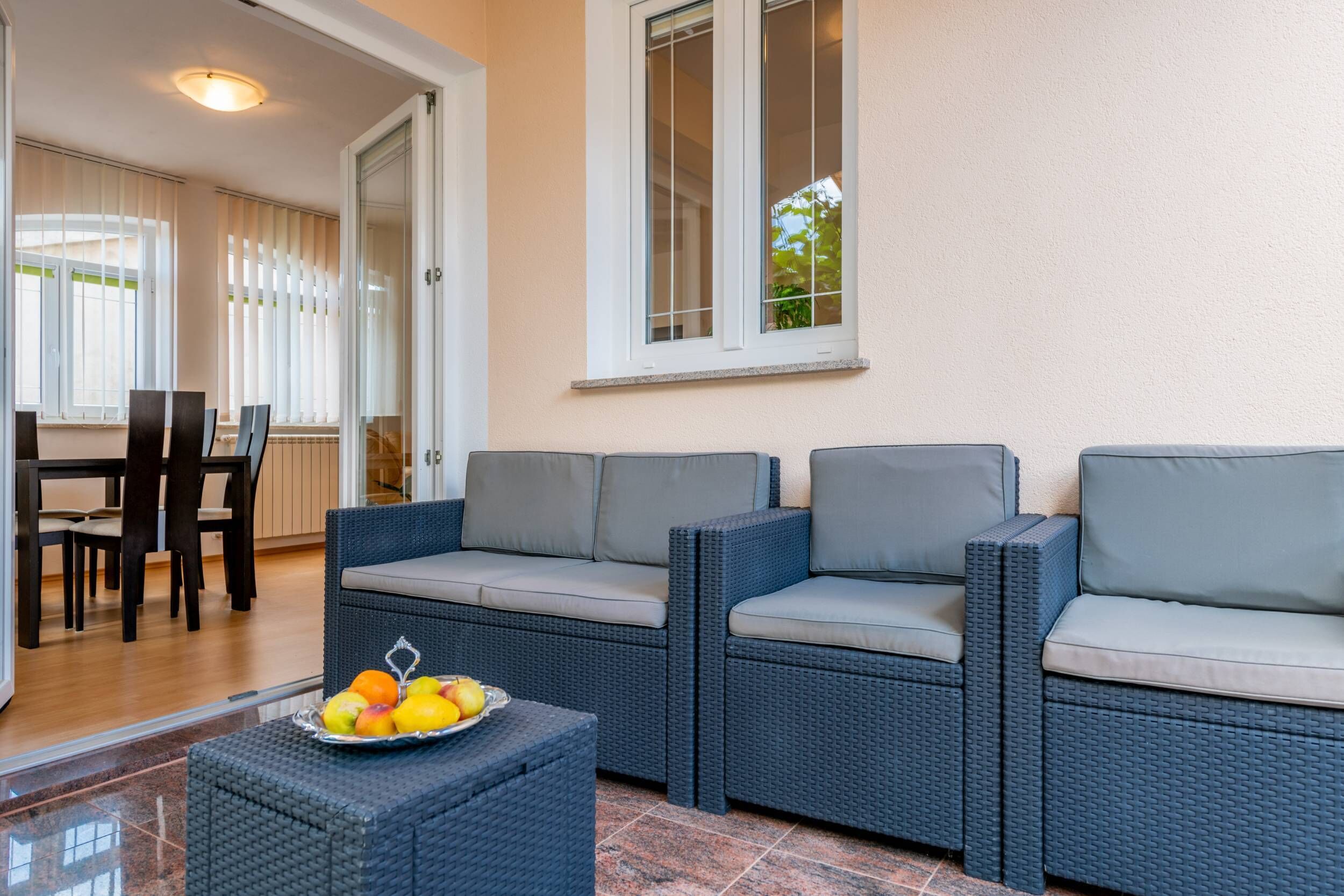 A patio area with wicker furniture, a fruit bowl, and a view of the interior.