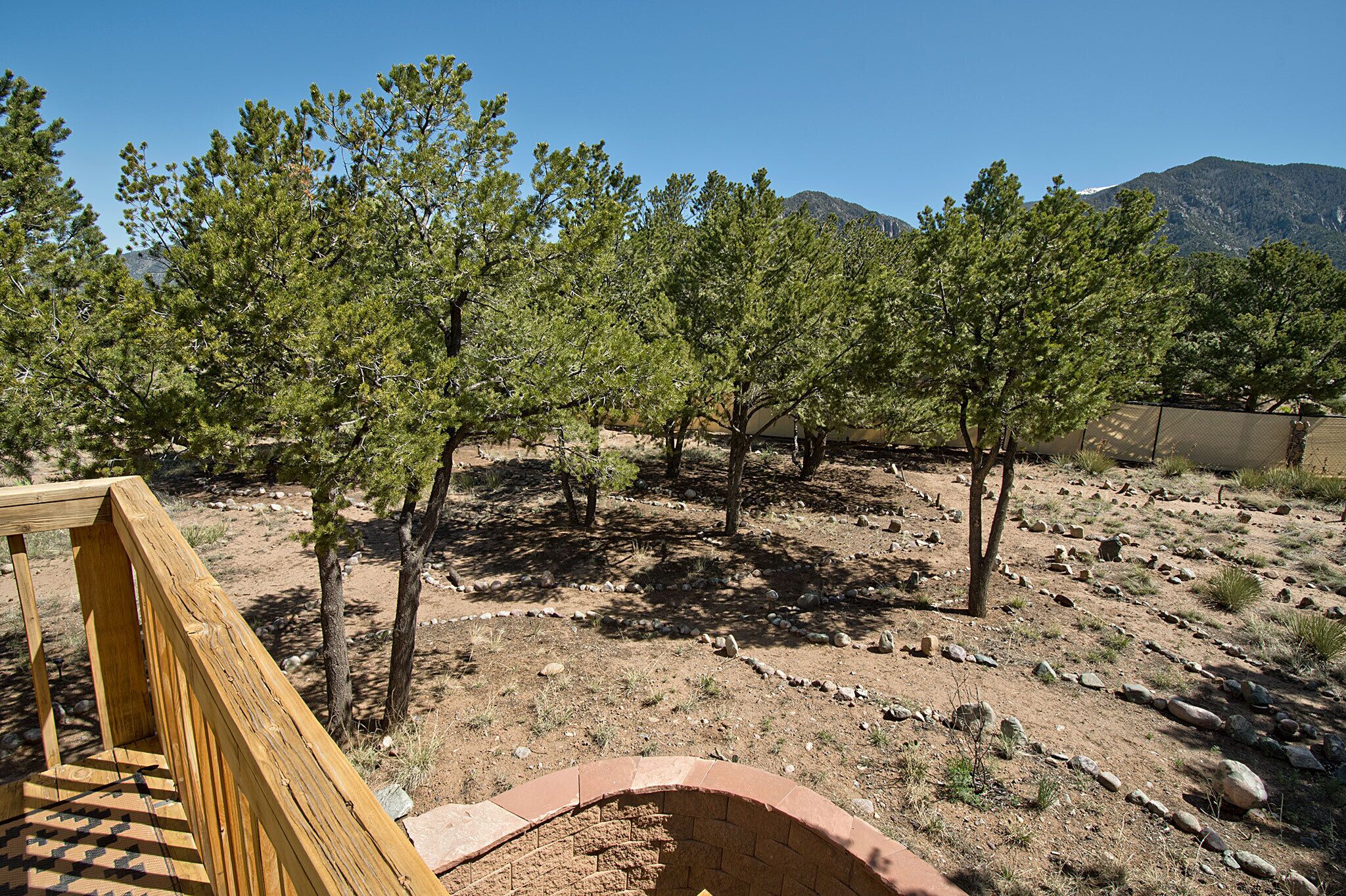 Une terrasse en bois avec un foyer en briques, entourée d’arbres et offrant une vue sur un paysage montagneux.
