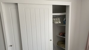 Un placard blanc avec une tringle et des étagères, une porte avec une poignée et une prise de courant sur le mur.