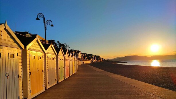 Une rangée de cabanes de plage, avec une promenade en béton qui mène à la plage.