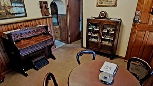 Un espace repas comprenant une table ronde, des chaises, un piano, un meuble avec des portes en verre et une porte sur laquelle est apposée une pancarte.