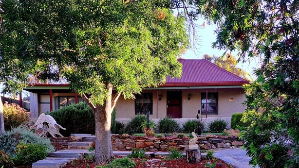 Une maison avec un toit rouge, un chemin de pierre et un jardin bien entretenu, agrémenté de diverses plantes et d’une statue.